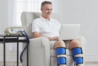 Man using Bio Compression Digital Arterial Pump with bilateral leg compression sleeves while sitting in a chair — high pressure rapid cycle arterial compression therapy for legs